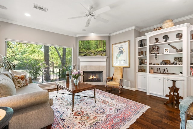 living room with a ceiling fan, a tile fireplace, visible vents, ornamental molding, and dark wood-type flooring