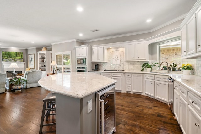 kitchen with beverage cooler, a kitchen bar, white cabinets, a sink, and appliances with stainless steel finishes