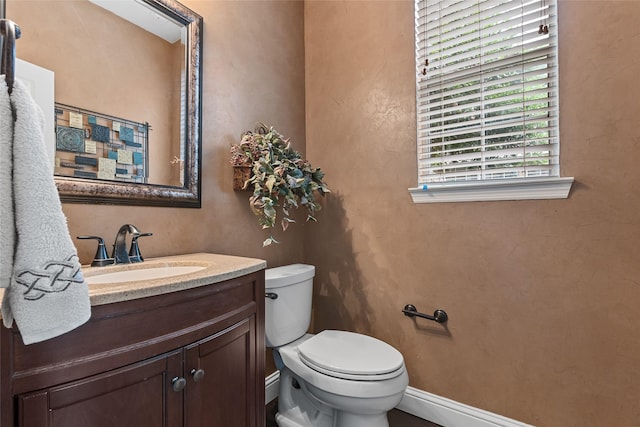 half bath with vanity, baseboards, and toilet
