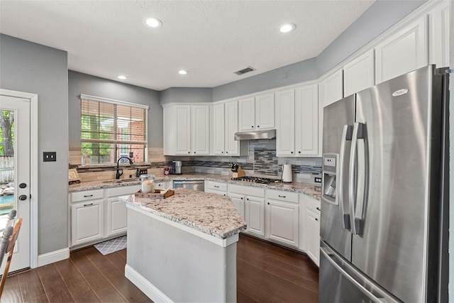 kitchen with a sink, stainless steel appliances, under cabinet range hood, visible vents, and dark wood-style floors