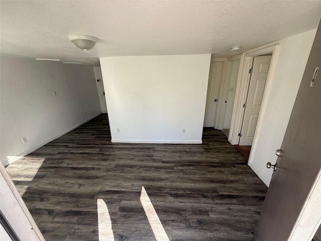 empty room featuring a textured ceiling, baseboards, and dark wood-type flooring