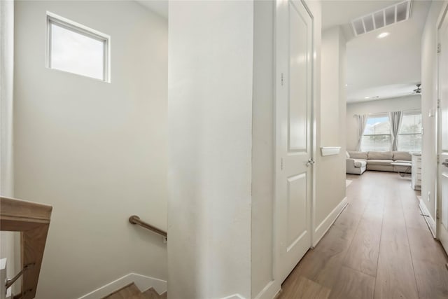 hallway with baseboards, an upstairs landing, light wood-type flooring, and visible vents