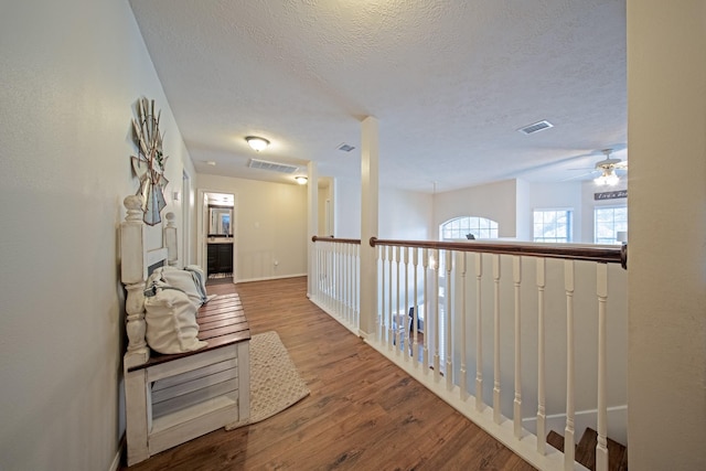 hall featuring visible vents, a textured ceiling, and wood finished floors