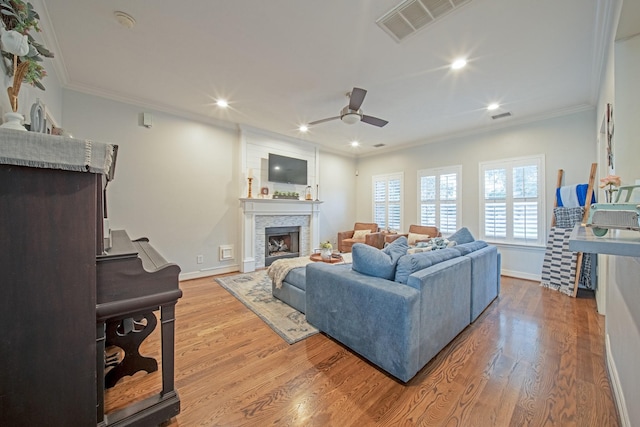 living area featuring crown molding, ceiling fan, visible vents, and a stone fireplace