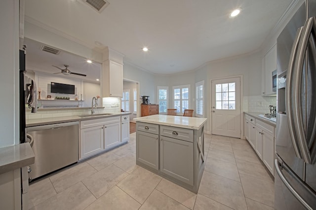 kitchen featuring appliances with stainless steel finishes, a sink, tasteful backsplash, a kitchen island, and visible vents