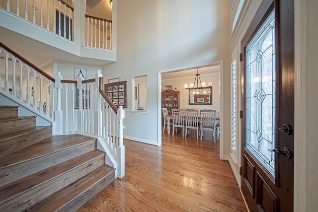 foyer entrance with wood finished floors, baseboards, a high ceiling, stairway, and a notable chandelier