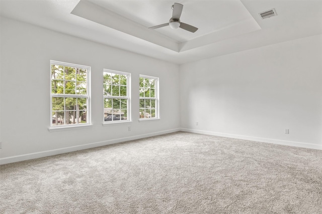 carpeted spare room featuring a raised ceiling, ceiling fan, baseboards, and visible vents
