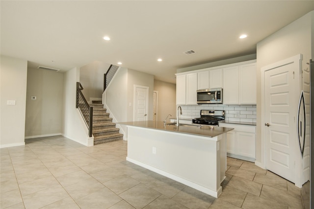 kitchen with decorative backsplash, white cabinets, a sink, light tile patterned floors, and stainless steel appliances