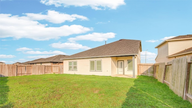 rear view of property with a lawn, a shingled roof, and a fenced backyard