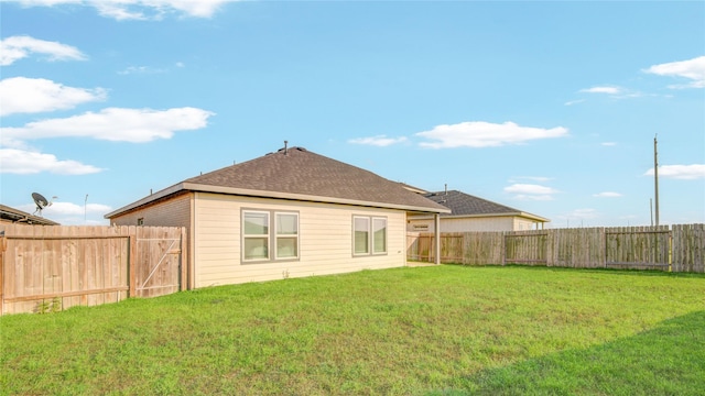 back of house with a fenced backyard, a shingled roof, and a yard