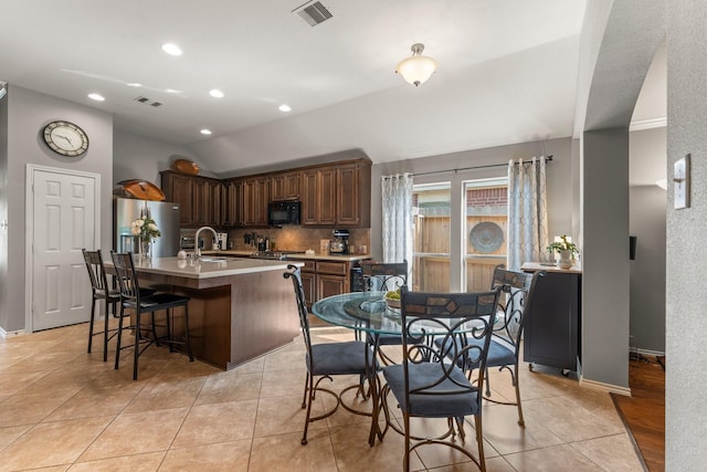kitchen featuring visible vents, black microwave, stainless steel fridge with ice dispenser, a sink, and backsplash
