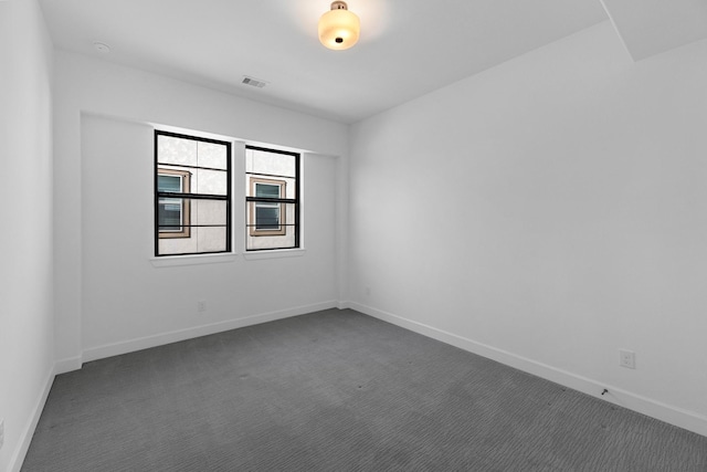 spare room with baseboards, visible vents, and dark carpet