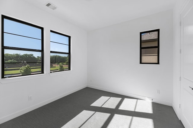 unfurnished room with plenty of natural light, dark colored carpet, and visible vents