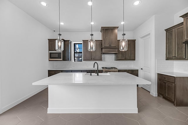 kitchen featuring dark brown cabinets, appliances with stainless steel finishes, a sink, backsplash, and a center island with sink