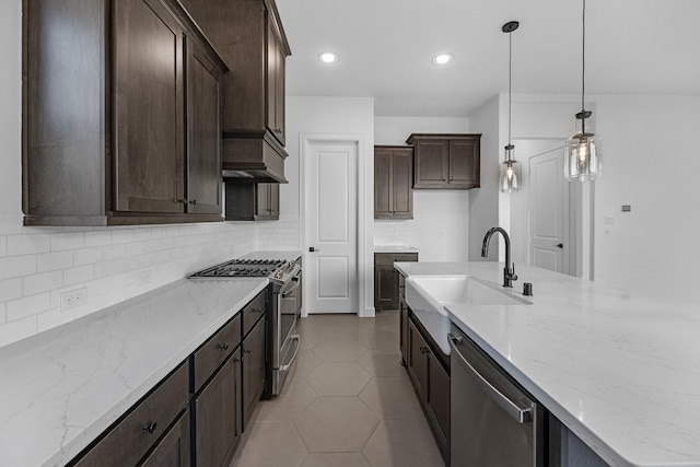 kitchen featuring dark brown cabinets, light stone counters, appliances with stainless steel finishes, a sink, and tasteful backsplash