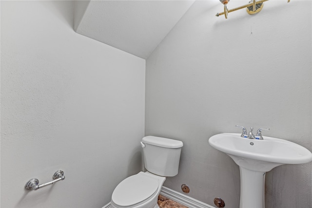 half bathroom with baseboards, vaulted ceiling, and toilet