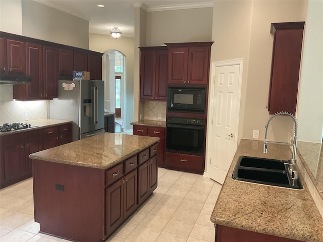 kitchen featuring a sink, decorative backsplash, arched walkways, and black appliances
