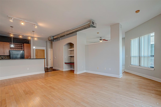 unfurnished living room featuring a ceiling fan, baseboards, track lighting, and light wood-style floors