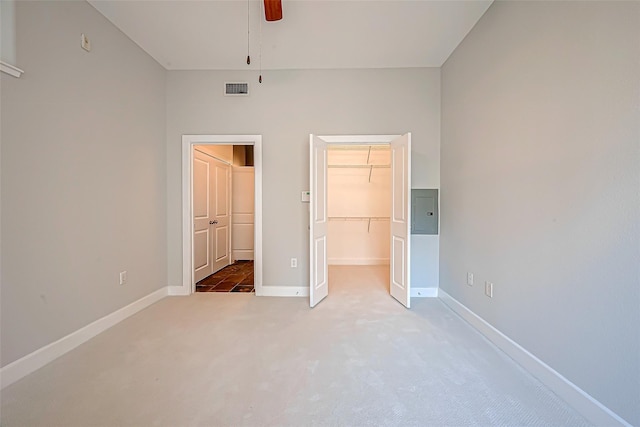 unfurnished bedroom with visible vents, baseboards, a walk in closet, light colored carpet, and electric panel