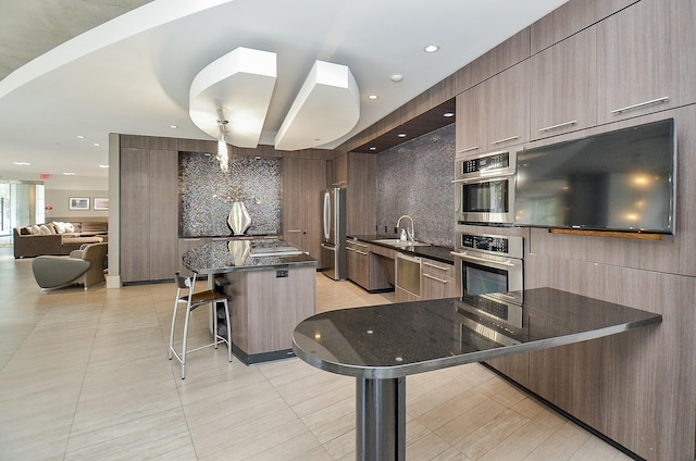 kitchen with decorative backsplash, a kitchen island, a breakfast bar, modern cabinets, and dark stone countertops