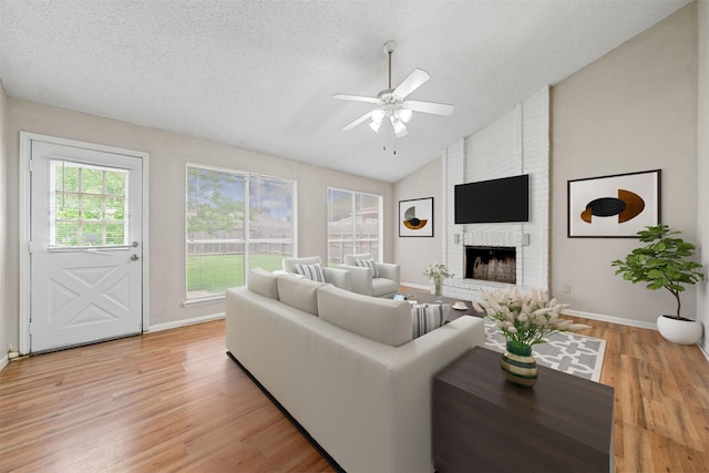 living area featuring ceiling fan, a brick fireplace, a textured ceiling, lofted ceiling, and light wood-type flooring