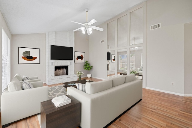 living room featuring visible vents, a ceiling fan, light wood finished floors, and a brick fireplace
