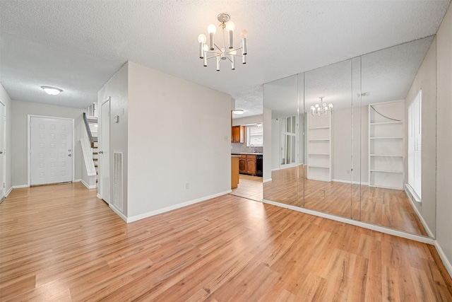 unfurnished living room featuring a textured ceiling, an inviting chandelier, and light wood finished floors