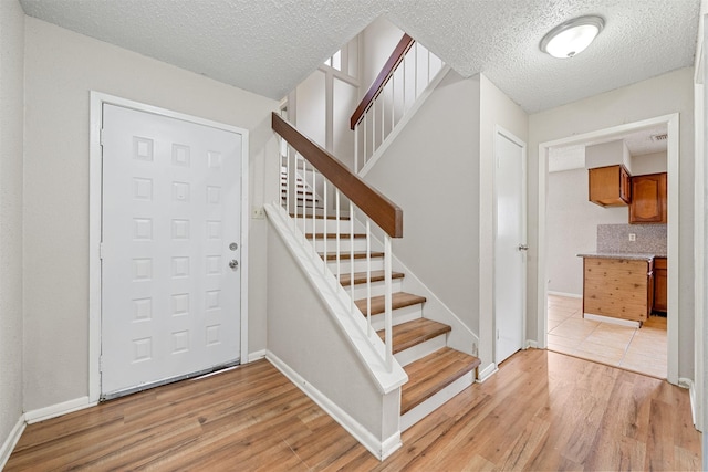 foyer entrance with a textured ceiling, baseboards, stairway, and light wood-style floors