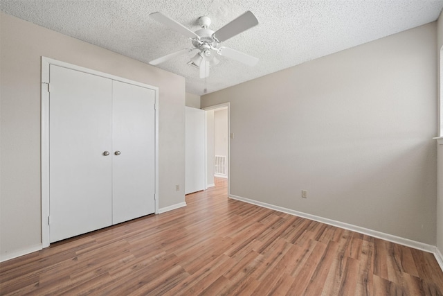 unfurnished bedroom with ceiling fan, light wood finished floors, a textured ceiling, baseboards, and a closet