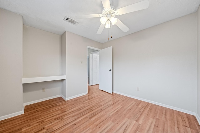spare room with baseboards, a ceiling fan, wood finished floors, and visible vents