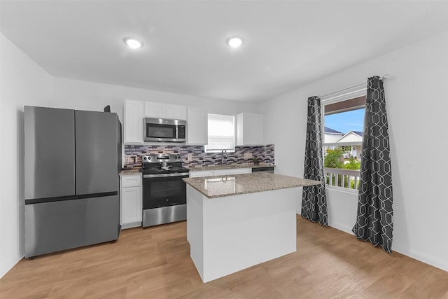 16435 Valerie Marie Pl, Conroe, TX 77306 - kitchen featuring decorative backsplash, a kitchen island, light stone counters, stainless steel appliances, and white cabinetry