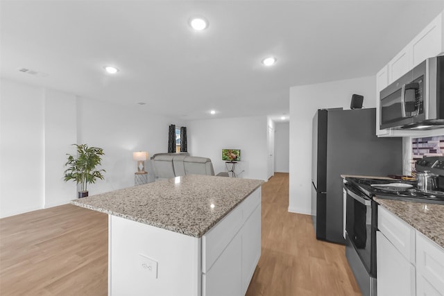 16435 Valerie Marie Pl, Conroe, TX 77306 - kitchen with visible vents, a kitchen island, light wood-type flooring, white cabinets, and appliances with stainless steel finishes