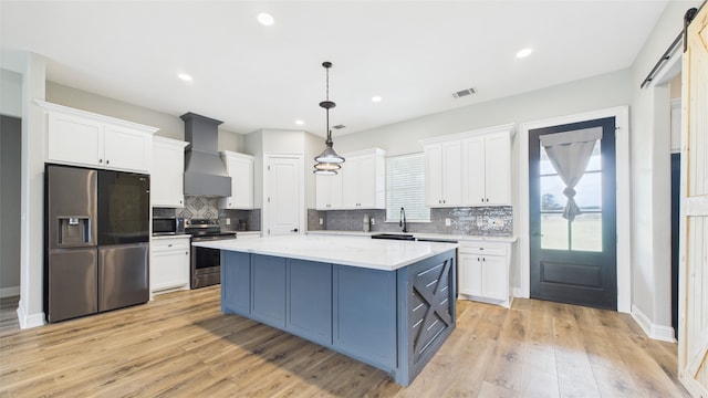 kitchen with wall chimney range hood, white cabinets, and appliances with stainless steel finishes