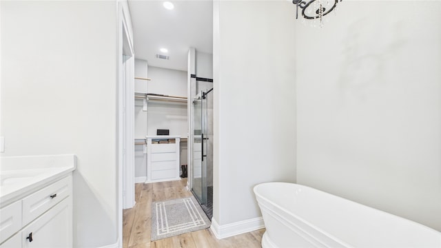 full bath featuring a freestanding tub, a shower stall, wood finished floors, vanity, and a spacious closet