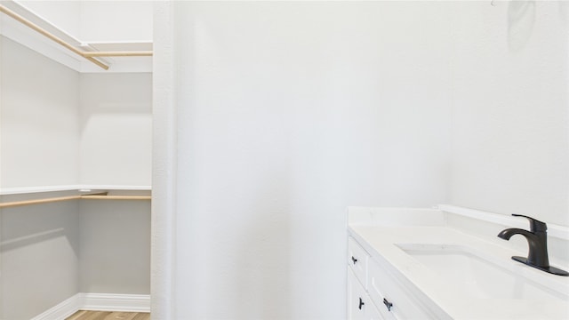 bathroom featuring a walk in closet, baseboards, vanity, and wood finished floors