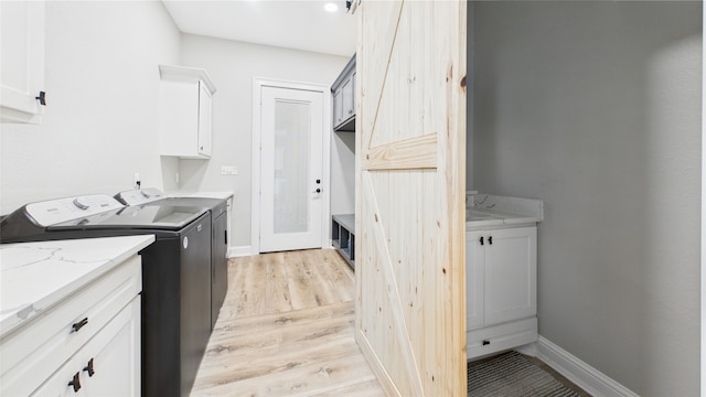 washroom featuring separate washer and dryer, cabinet space, baseboards, and light wood-style floors