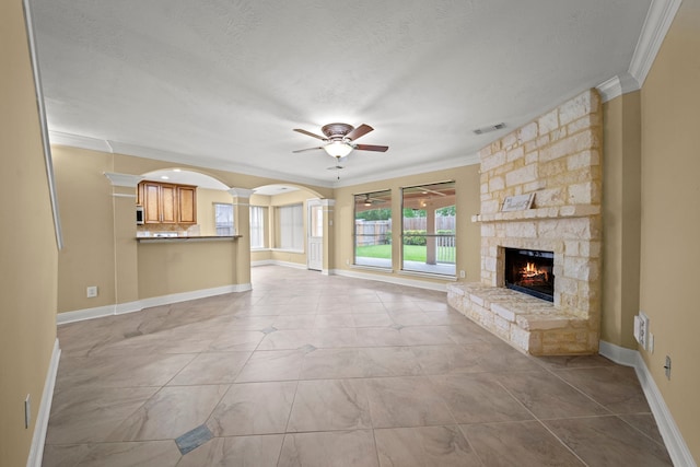 unfurnished living room featuring crown molding, ceiling fan, a stone fireplace, and visible vents