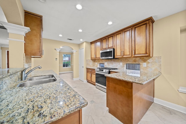 kitchen featuring brown cabinets, a sink, stainless steel appliances, a peninsula, and ornate columns