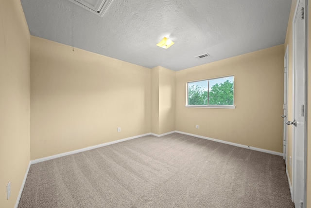 carpeted spare room with baseboards, attic access, a textured ceiling, and visible vents