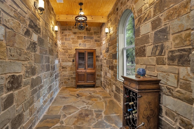 wine cellar with stone flooring, arched walkways, wooden ceiling, and beamed ceiling