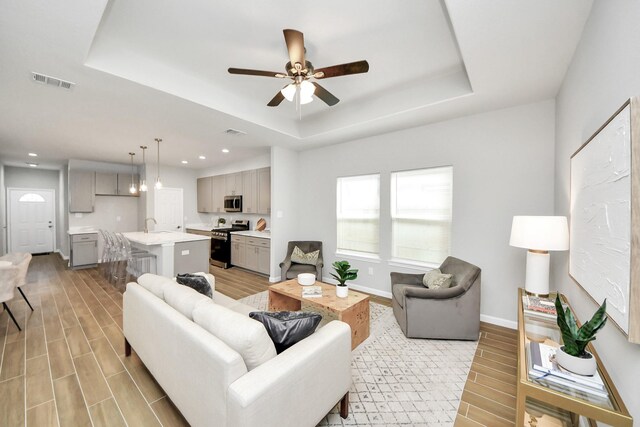 326 Gans St Unit A, Houston, TX 77029 - living room featuring visible vents, light wood-style floors, baseboards, a tray ceiling, and a ceiling fan