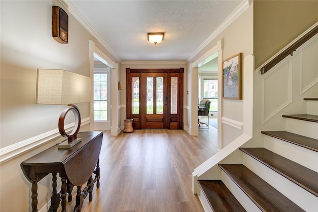 foyer entrance with a textured ceiling, crown molding, wood finished floors, baseboards, and stairs