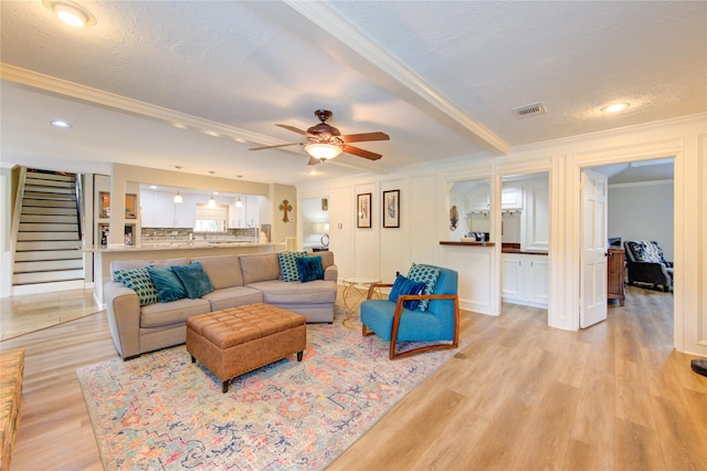 living room featuring visible vents, ornamental molding, stairs, ceiling fan, and light wood-type flooring