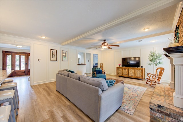 living area featuring ornamental molding, light wood-style flooring, a ceiling fan, and a decorative wall