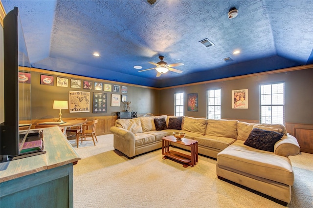 carpeted living area featuring a ceiling fan, wainscoting, a tray ceiling, and a wealth of natural light