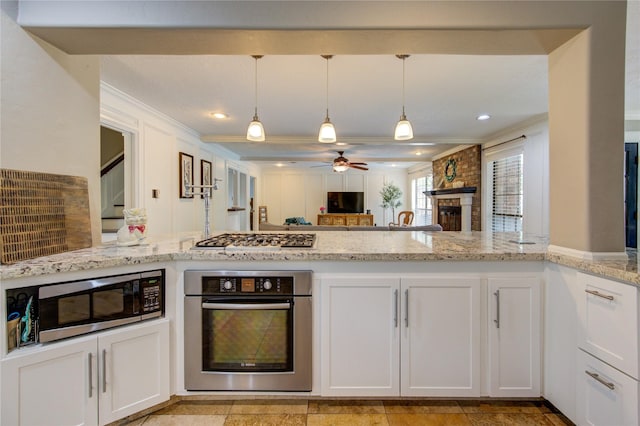 kitchen featuring crown molding, open floor plan, light stone counters, a ceiling fan, and appliances with stainless steel finishes