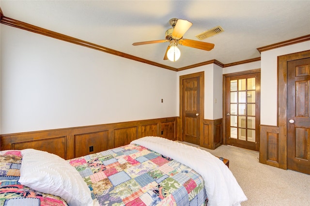 carpeted bedroom with visible vents, a ceiling fan, wainscoting, and crown molding