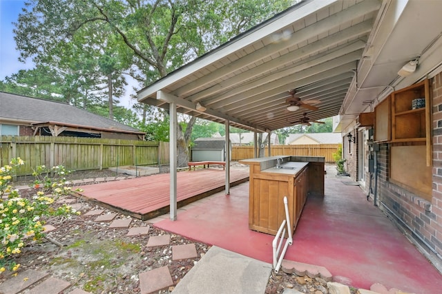 view of patio with ceiling fan, a wooden deck, a sink, a fenced backyard, and an outdoor kitchen