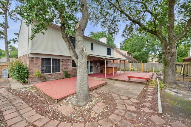 back of property with brick siding, a wooden deck, a fenced backyard, and a chimney