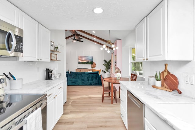 kitchen featuring white cabinetry, open floor plan, vaulted ceiling with beams, stainless steel appliances, and light wood-style flooring